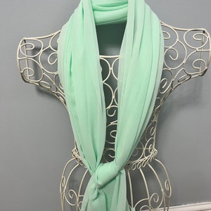May include: A light green chiffon scarf draped over a white wire mannequin. The scarf is folded in half and tied in a knot at the front.