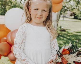 Op de afbeelding: Een jong meisje in een witte kanten jurk houdt een boeket gedroogde bloemen vast in herfstkleuren. Het boeket bevat gedroogde bladeren, pampasgras en varens.