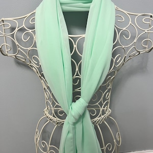 May include: A light green chiffon scarf draped over a white metal mannequin. The scarf is tied in a knot at the front.