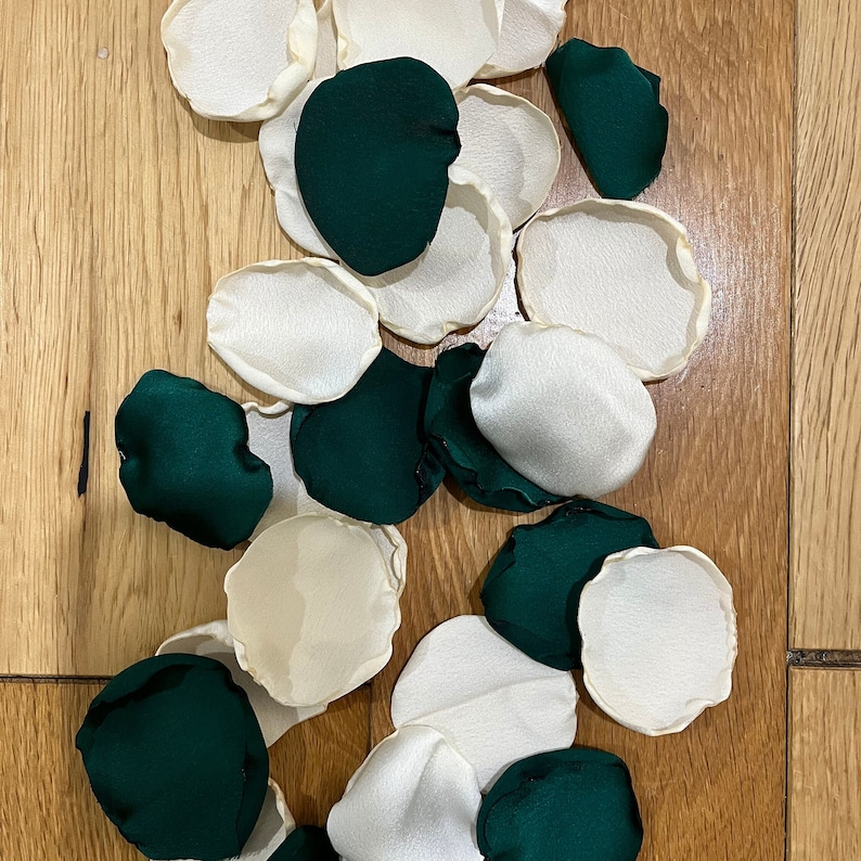 Op de afbeelding: Een verzameling groene en witte stoffen rozenblaadjes. De blaadjes zijn willekeurig gerangschikt op een houten oppervlak.