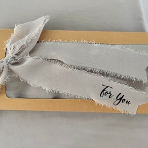 May include: A brown cardboard box with a clear window, decorated with a gray frayed ribbon and the text "For You".