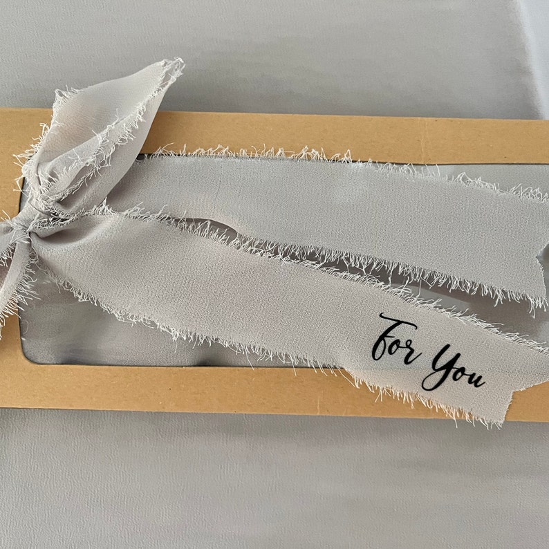 May include: A brown cardboard box with a clear window, decorated with a gray frayed ribbon and the text "For You".