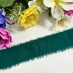 Könnte beinhalten: Ein dunkelgrünes Stoffband mit ausgefransten Kanten. Das Band liegt auf einer weißen Oberfläche.