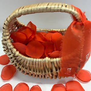 May include: A wicker basket filled with orange fabric flower petals. The basket has a handle and a fabric tag with the name "Ava" on it.