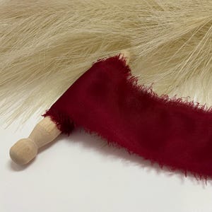 May include: A wooden dowel with a burgundy silk ribbon wrapped around it. The ribbon has a frayed edge.