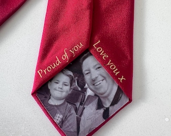 May include: A deep red necktie featuring a black and white photograph of a child and an adult printed on the fabric. The text "Proud of you" is embroidered on the left side and "Love you x" is embroidered on the right side in gold thread.