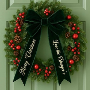 May include: A festive Christmas wreath featuring evergreen foliage, red berries, and pine cones. A dark green velvet bow is at the top, with the phrases "Merry Christmas" and "Love the Stringer's" printed on the ribbons.