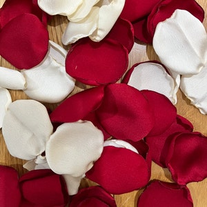 Può includere: Una collezione di petali di rosa in tessuto rosso e bianco. I petali sono disposti in modo casuale su una superficie di legno.