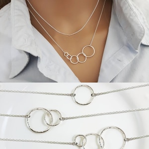 May include: Four silver circle necklaces with a hammered finish. The necklaces are layered on a white surface. The top necklace has four circles, the second has two circles, the third has three circles, and the bottom has four circles.