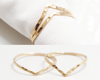 May include: Two gold hammered chevron rings. The rings are thin and delicate, and they are stacked on top of each other.
