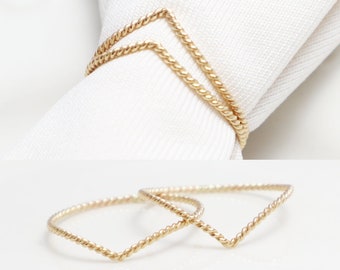 May include: Two gold-toned, twisted wire rings with a V-shaped design. The rings are stacked on top of each other.