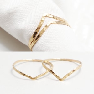 May include: Two gold hammered chevron rings. The rings are thin and delicate, and they are stacked on top of each other.
