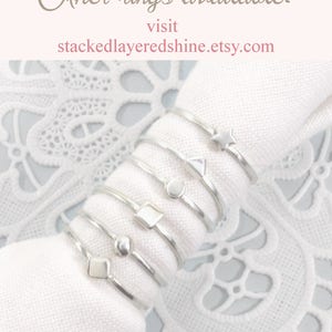 Puede incluir: Un conjunto de anillos apilables de plata con diferentes formas geom&eacute;tricas, incluyendo una estrella, un tri&aacute;ngulo, un c&iacute;rculo, un cuadrado y una cuenta. Los anillos se muestran sobre un fondo de tela blanca. &iexcl;Otros anillos disponibles! Visita stackedlayeredshine.etsy.com