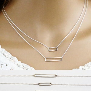 May include: A silver necklace with two rectangular pendant charms. The larger charm is longer and thinner than the smaller charm.