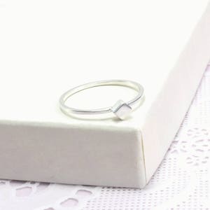 Puede incluir: Un anillo de plata simple con un acento de forma cuadrada. El anillo es delgado y delicado.