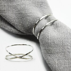 May include: Two silver rings, one is a simple band and the other is a criss-cross design. Both rings have a hammered texture.