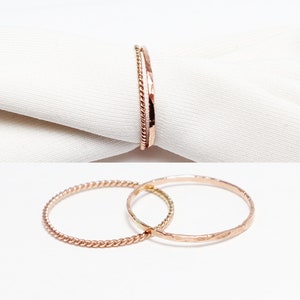Puede incluir: Dos anillos de oro delicados, uno con un diseño trenzado y el otro con un acabado martillado.