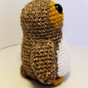 May include: A brown and white crocheted owl plush toy with black eyes. The owl has a yellow beak and feet.