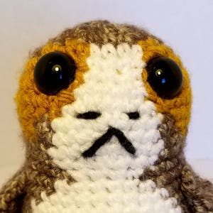 May include: A crocheted stuffed toy with brown, white and orange fur. The toy has large black eyes and a small black mouth.