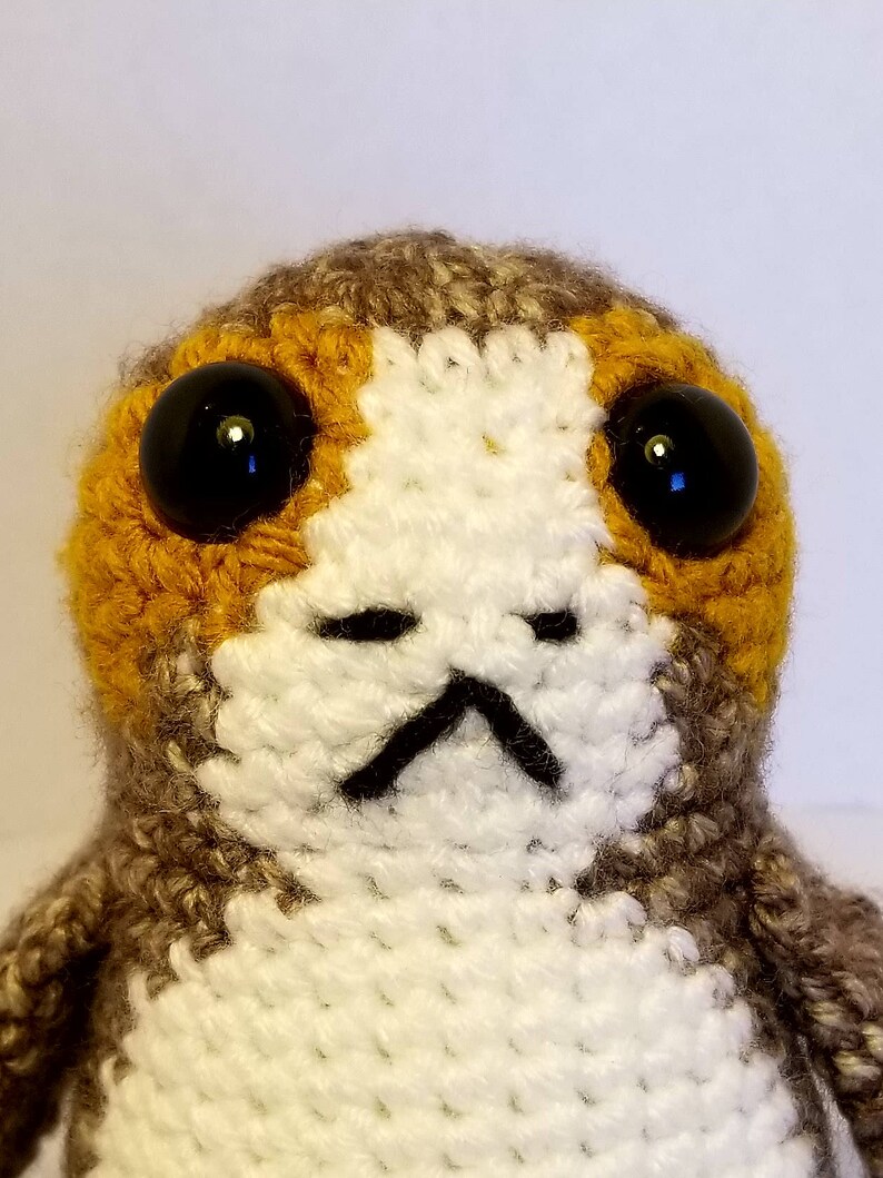 May include: A crocheted stuffed toy with brown, white and orange fur. The toy has large black eyes and a small black mouth.