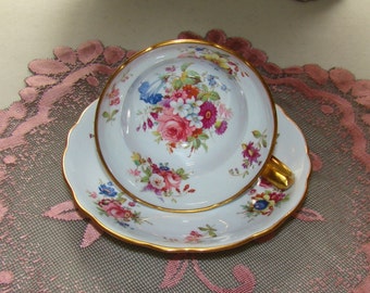 May include: A white teacup and saucer with a floral pattern in shades of pink, blue, yellow, and green. The cup and saucer have a gold trim.