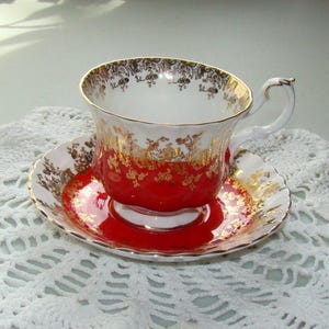 May include: A red and gold teacup and saucer set with a floral pattern. The saucer has a scalloped edge.