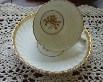 May include: A white teacup and saucer with a gold rim and a gold floral design. The saucer has a scalloped edge.