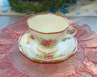 May include: A white teacup and saucer with a gold rim and floral pattern. The floral pattern features pink, red, and purple flowers.