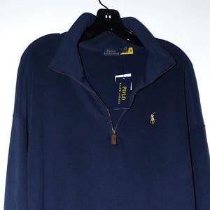 May include: Navy blue long-sleeve dress with a quarter-zip neckline. The dress features a small embroidered logo on the chest and a tag with the brand name. The dress is hanging on a black hanger.