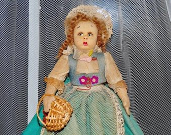 May include: A vintage cloth doll with red hair, wearing a blue and green dress with a white lace trim and a basket in her hand.