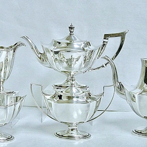 May include: A silver tea set with a teapot, creamer, sugar bowl, and a matching teacup. The set is in a traditional style with a rounded shape and a polished finish.