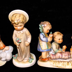 May include: A collection of ceramic figurines depicting religious scenes. The figurines include angels, children, and a baby in a manger. The figures are painted in soft, muted colors with detailed features. The figurines are likely part of a nativity set.