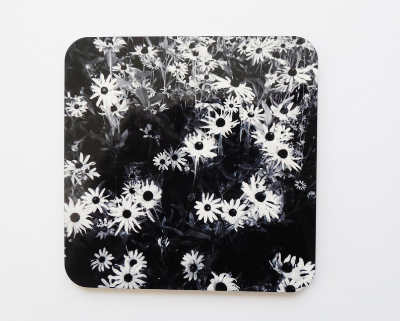 K&ouml;nnte beinhalten: Schwarz-wei&szlig;er Untersetzer mit einem floralen Design mit wei&szlig;en G&auml;nsebl&uuml;mchen auf schwarzem Hintergrund.