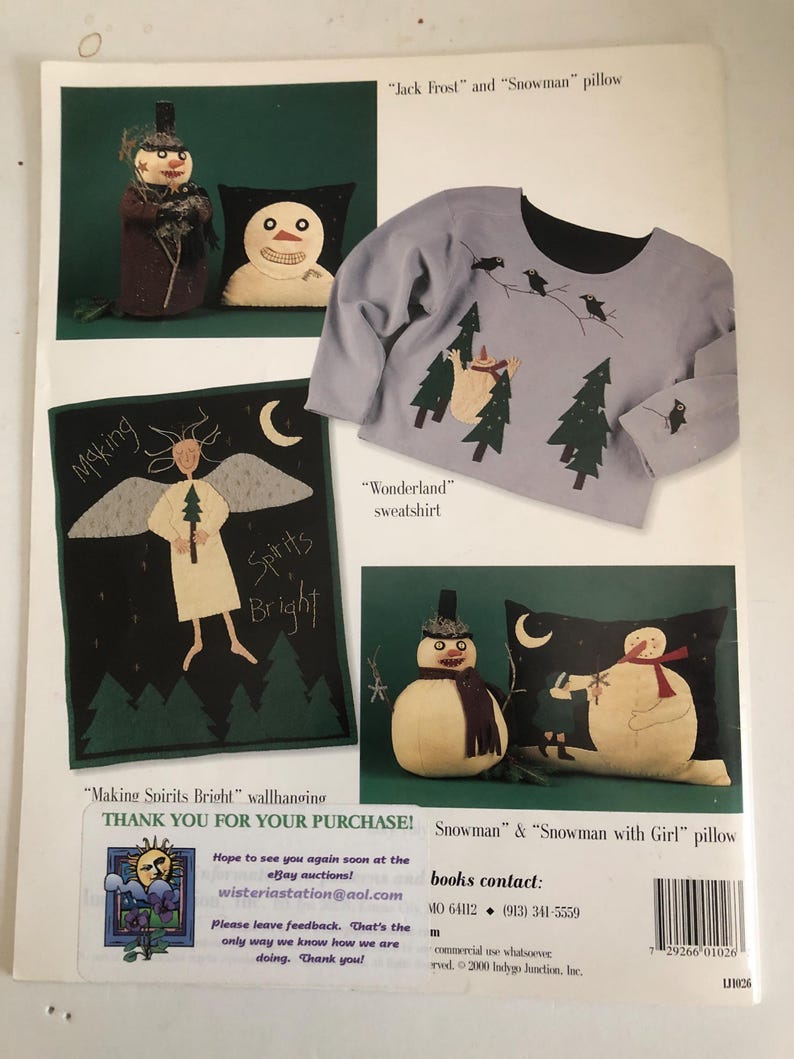 May include: A page featuring winter-themed crafts. It includes a gray sweatshirt with a black collar and a design of trees and birds. There are also snowman pillows and a wall hanging with an angel and the words "Making Spirits Bright."