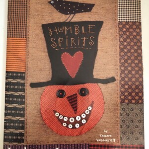 May include: A decorative fabric panel featuring a smiling pumpkin wearing a black top hat with the words "Humble Spirits." A black bird sits atop the hat. The panel has a patchwork design with various patterns and the text "Indygo Junction, Inc."