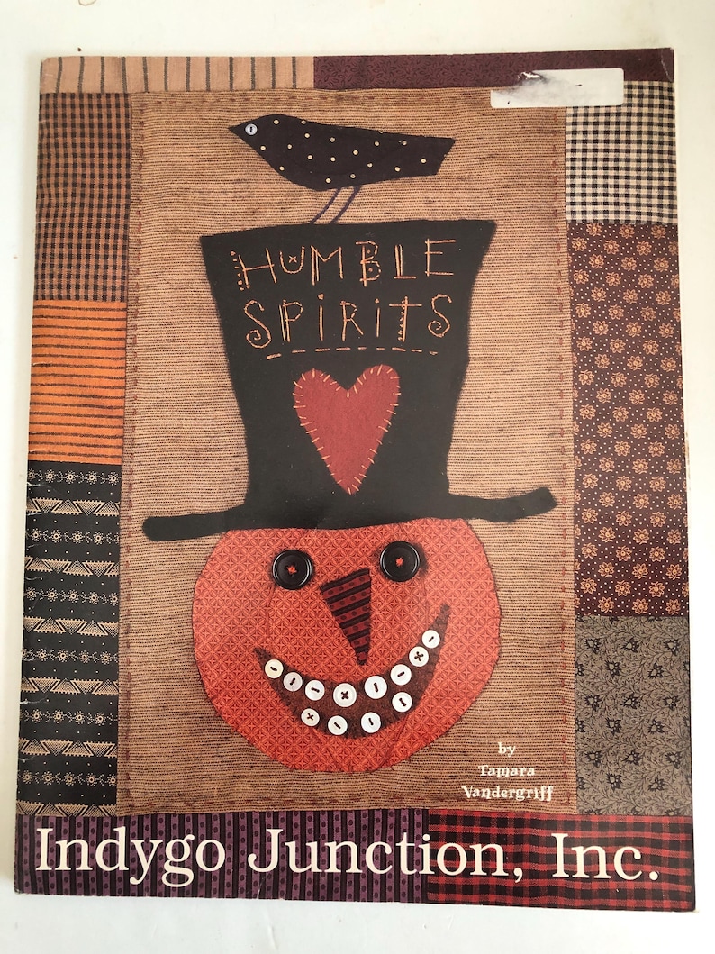 May include: A decorative fabric panel featuring a smiling pumpkin wearing a black top hat with the words "Humble Spirits." A black bird sits atop the hat. The panel has a patchwork design with various patterns and the text "Indygo Junction, Inc."