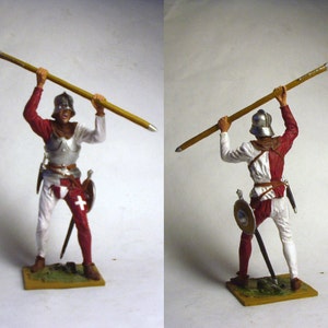 Puede incluir: Figura en miniatura de un soldado medieval con armadura roja, blanca y plateada, sosteniendo una alabarda. El soldado lleva un casco y porta un escudo y una espada. La figura está sobre una pequeña base rectangular.