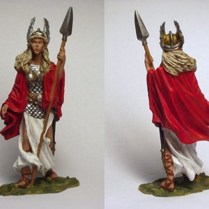Puede incluir: Figura detallada de una mujer guerrera, vestida con una capa roja y armadura plateada, sosteniendo una lanza. La figura lleva un casco alado y un vestido blanco. La base está pintada de verde, sugiriendo un terreno herboso.