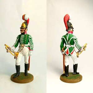 May include: A painted figurine of a soldier wearing a green and white uniform with a red and white plumed hat. The soldier is holding a bugle and a sword.