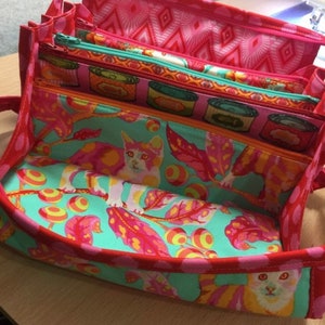 May include: A red fabric organizer with multiple pockets and zippers. The organizer is lined with a turquoise fabric featuring a pattern of cats, leaves, and circles.