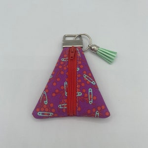 May include: A small triangular zippered pouch with a purple background and a pattern of red cherries and light blue safety pins. The pouch has a silver zipper and a light green tassel attached to a silver key ring.