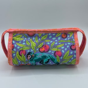 May include: A rectangular fabric bag with a colorful pattern featuring a teal monkey, red cherries, and green leaves on a purple background. The bag has pink handles and trim.