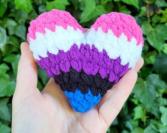 May include: A crocheted heart-shaped plush toy in the colours of the non-binary pride flag: pink, white, purple, black, and blue.
