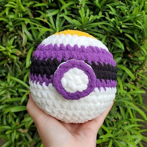 Op de afbeelding: Een gehaakte bal met paarse, zwarte, witte en gele strepen. De bal heeft een grote paarse cirkel in het midden.