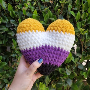 Peut inclure: Un coussin en forme de cœur crocheté avec des rayures jaunes, blanches, violettes et noires.