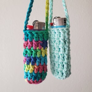 May include: Two crocheted lighter holders, one in a rainbow pattern and one in a light blue color. Both holders have a silver lighter inside.
