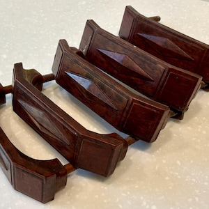 Op de afbeelding: Een set van vier donkerbruine ladehandgrepen met een rechthoekige vorm en een centraal verhoogd ruitvormig detail. Elke handgreep heeft een gladde afwerking en is voorzien van twee metalen draadeinden aan de achterzijde voor montage.