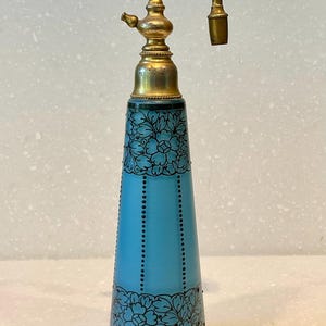 May include: A vintage blue glass perfume bottle with a gold metal spray top and black floral design.