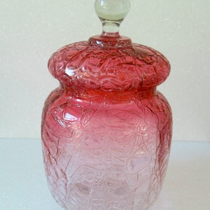 May include: A vintage glass jar with a textured, frosted finish. The jar is a gradient of pink and clear glass with a clear glass knob lid.