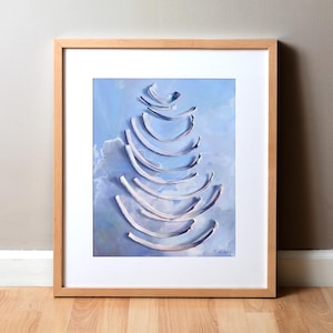 May include: Framed artwork featuring a stylized, white ribcage shape against a light blue sky with clouds. The artwork is in a light wood frame, creating a minimalist aesthetic. The painting has a surreal, dreamlike quality.